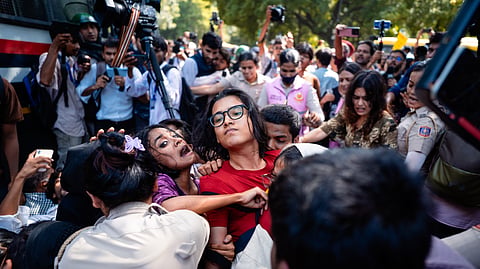 Neha Bora in a red Tshirt being detained by security personnel at a protest