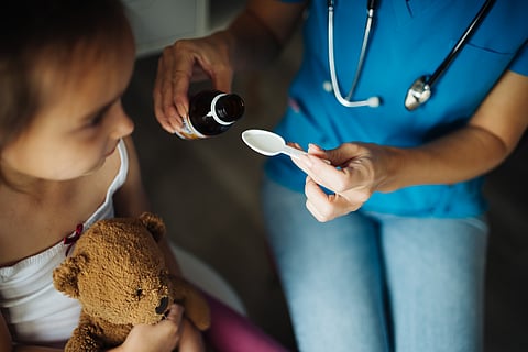 a female doctor giving oral medicine to a child. The child carries a doll