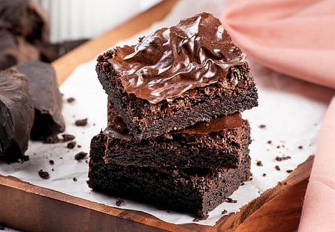 A picture of three brownie squares stacked on top of each other with crumbs on the table