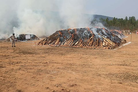 A police man using a long stick to ensure that the ganja is burnt on the pyre