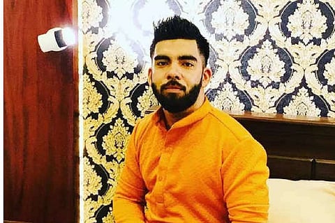 Aboobacker Siddique wearing a saffron colored kurta, against a backdrop of curtain with floral designs