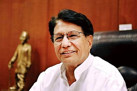 Ajit Singh sits on a chair against a wooden panel with a statue on his left