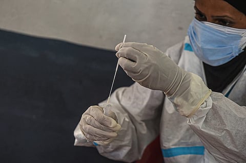 A health worker wearing PPE holding a COVID-19 test swab