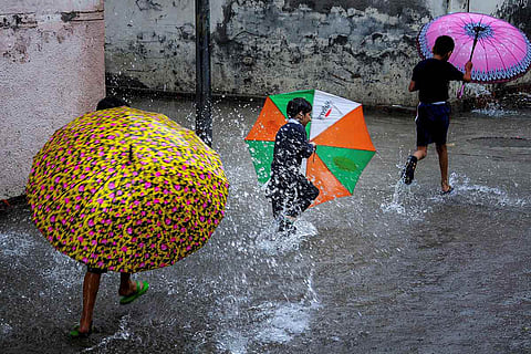 Three children holding colourful umbrellas and jumping in puddles