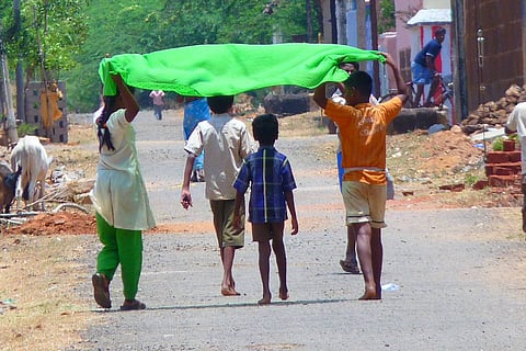 A group of children hold up a piece of cloth to shield themselves from the sun