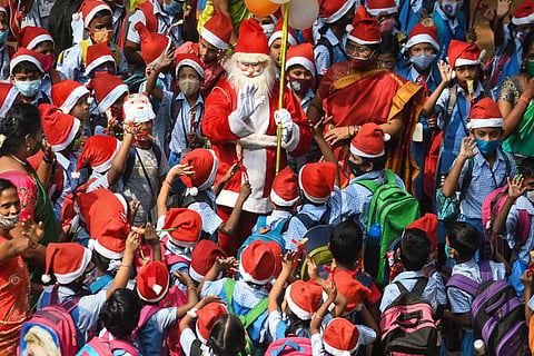 A man dressed as Santa Claus surrounded by school children wearing red hats