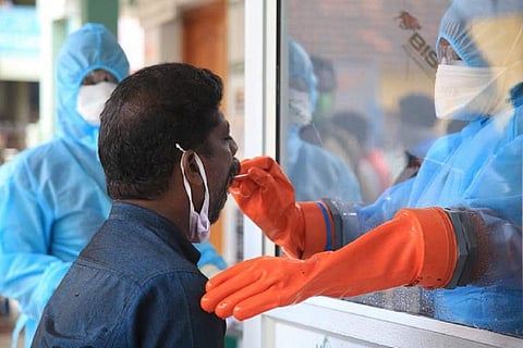 A man getting a COVID-19 test done by a health worker wearing a blue PPE suit and orange latex gloves