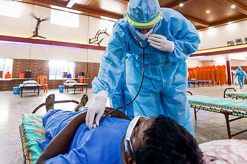 A doctor in a PPE suit checking a COVID-19 patient