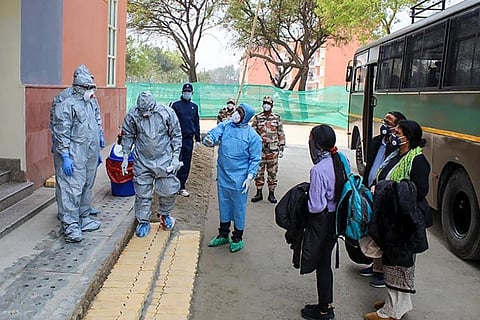 Medical professionals in PPE kits standing before a hotel
