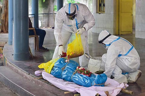 People wearing PPE kit keeping flowers on a dead body of a COVID-19 victim before cremation