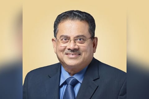 MG George Muthoot is smiling in this picture. He is wearing a black blazer, and a blue shirt and tie.