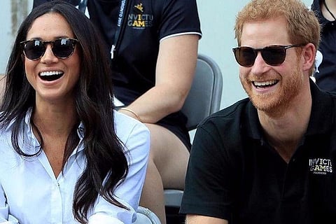 Harry in a black shirt and Meghan in a blue shirt