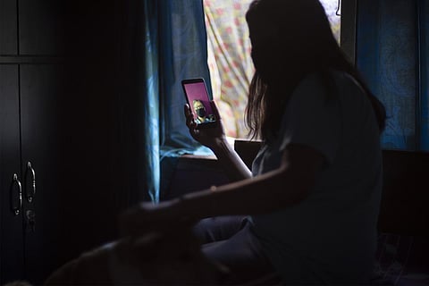 A woman in darkness does a video call with an eldery man at her home as a curtain flutters in the background