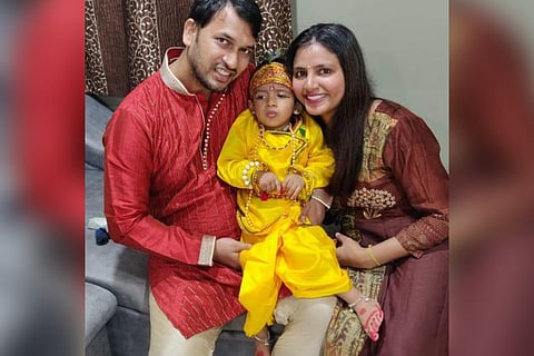 Ayaansh, dressed in Krishna's costume, seated between his parents