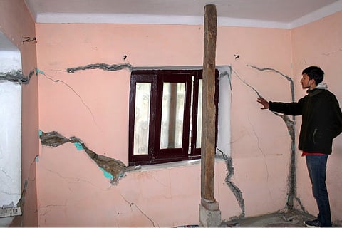 A person standing next to large cracks on the wall of a house