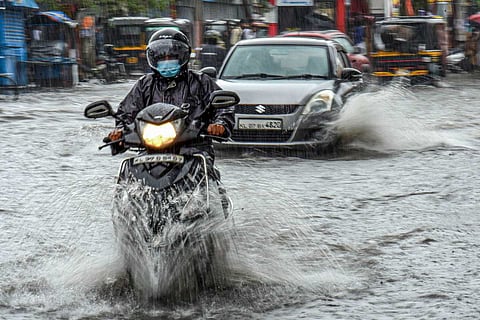 Commuters wade through a waterlogged road during monsoon rains, in Kochi