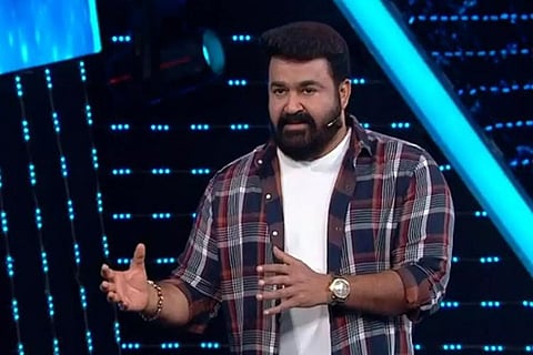 Mohanlal is seen wearing a white tee and multicoloured checked shirt and is seen hosting Bigg Boss in the image.