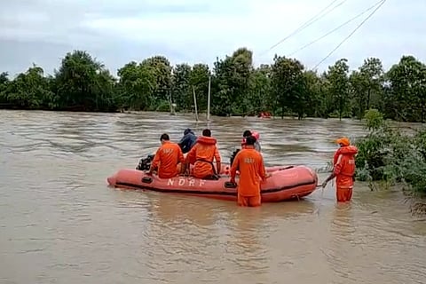 Four NDRF officials in a rescue raft on a flooded river