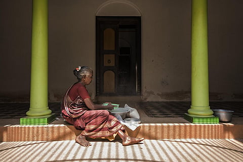 An old woman sits by a corridor doing household chores