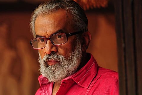 Malayalam actor P Balachandran wearing a red shirt and glasses