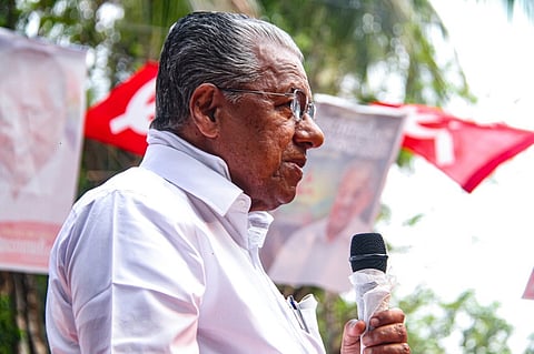 Kerala Chief Minister Pinarayi Vijayan standing and speaking at an Assembly election rally holding a mike against the background of a red flag