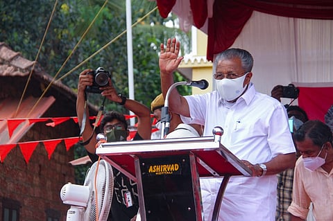 Kerala CM Pinarayi Vijayan addressing a poll rally waving, wearing mask, standing in front of a mic