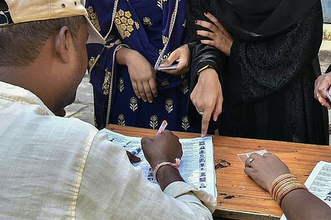 An election official checks a voter list on a wooden table while women stand nearby pointing at entries on the document. Image used for representation.