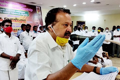 Tamil Nadu Minister for Higher Education K Ponmudy addressing a gathering wearing gloves and mask pulled down
