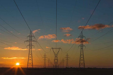 Power lines located against the backdrop of sun setting in the left corner and a blue sky