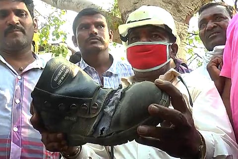 worker at hutti gold mines holds up torn boots