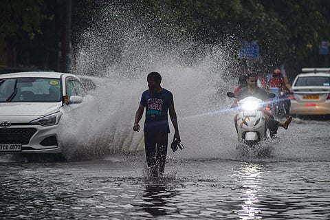 A man walking through a flooded road as vehicles pass by