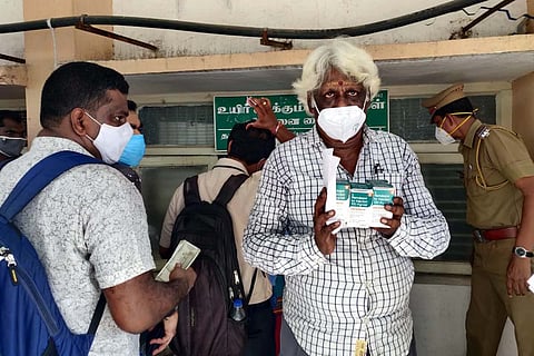 Man at a sales counter wearing white mask, holding three boxes of Remdesivir