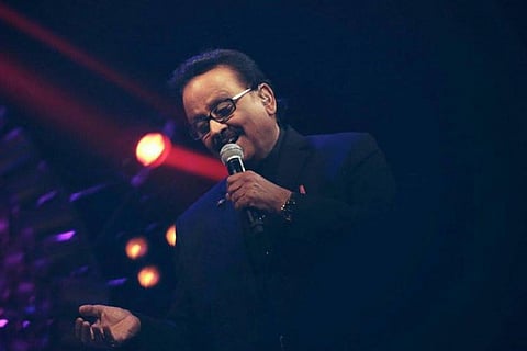 SP Balasubrahmanyam smiling while singing with a mic in hand