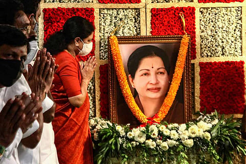Sasikala wearing an orange saree and a white mask prays to a picture of J Jayalalithaa