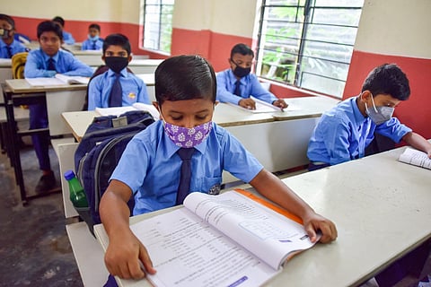 A group of school students sitting in a classroom with their masks on