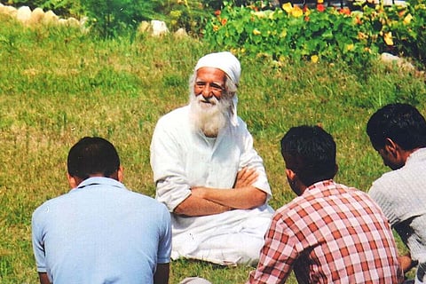 Sunderlal Bahuguna, wearing a white kurta and a white turban, sitting in the grass with three men sitting in front of him