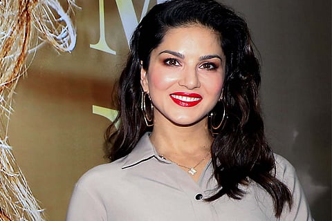 Sunny Leone wearing a grey shirt smiling looking ahead to the camera