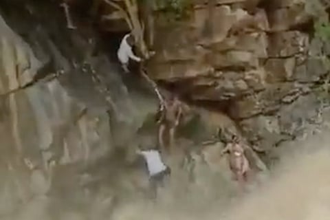 A rock above gushing water and rescue officials saving a mother and child using a rope