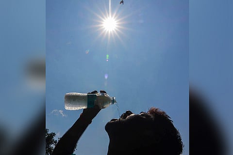 A representative image of a boy drinking water from a bottle and the sun in the background