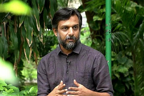 May 17 movement founder Thirumurgan Gandhi in a black shirt against a background of green foliage