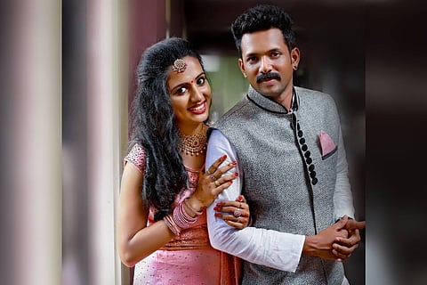 Vismaya in a pink dress holding the arms of her husband Kiran Kumar in a white shirt, grey jacket