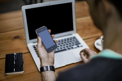 A person looking at their phone while working on a laptop