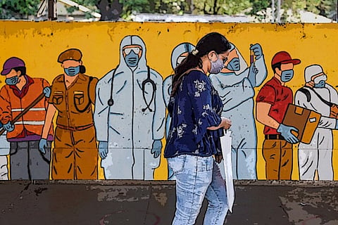 A woman wearing a mask walking in front of a mural of COVID-19 frontline workers