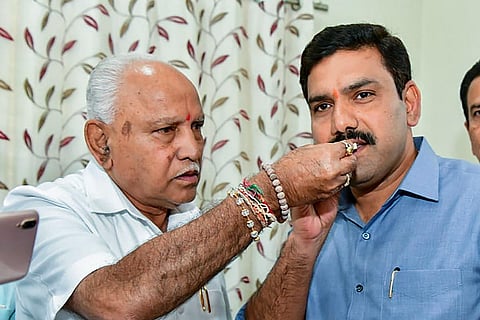 BS Yediyurappa hand feeding a sweet to his son BY Vijayendra