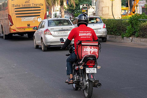 A Zomato delivery partner rides a bike on a busy road