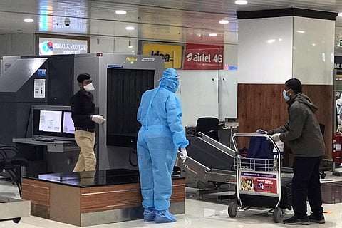 Official in PPE standing near conveyor belt in airport. A passenger standing near is taking bag from conveyor belt