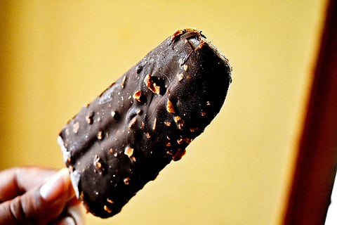 A hand holds a bar of chocolate-covered ice cream.