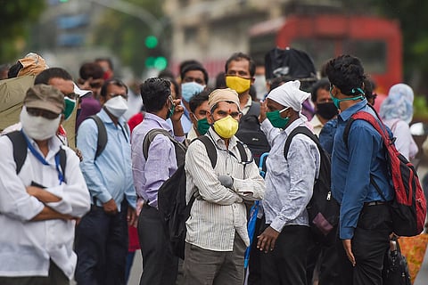 Men wearing masks wait for a bus in Mumbai