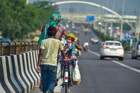 A woman walks with her son while her daughter is seated on a cycle that she is pushing