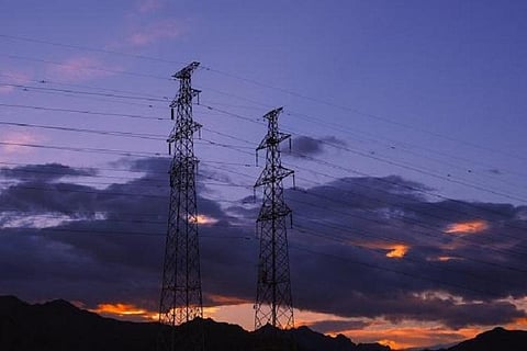 Electricity towers against a purple and orange sky at sunset